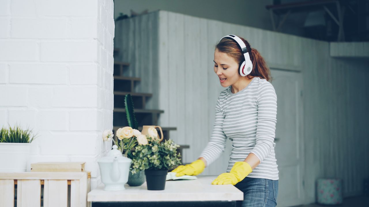 A woman with headphones cleaning indoors, surrounded by plants.
