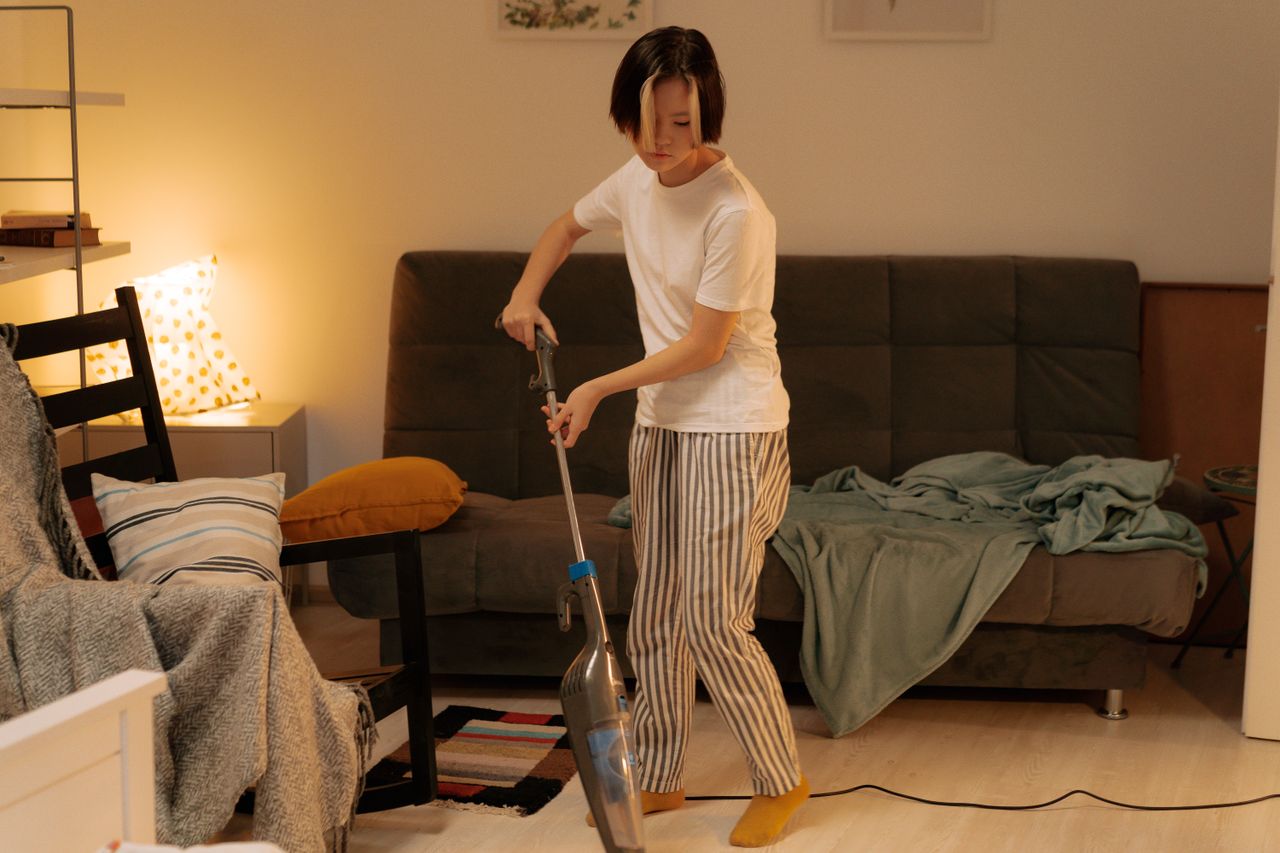 about-01 Asian woman cleaning a messy living room at home with a vacuum cleaner, creating a tidy space.